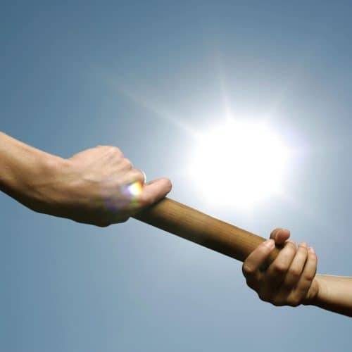 Close-up of hands passing a relay baton against a bright sunny sky.