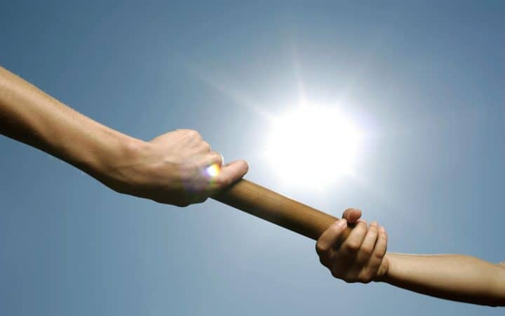Close-up of hands passing a relay baton against a bright sunny sky.