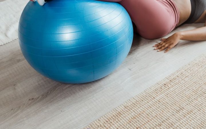 A woman working out at home with a blue stability ball and purple dumbbells for fitness.